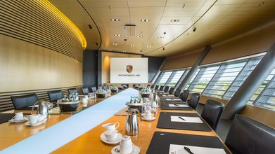 Großer Konferenzraum. Langer, breiter Massivholztisch. Edle Lederstühle. Große Leinwand. Moderne Holzvertäfelung. Kaffeservice. 