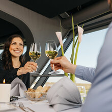 Frau prostet einem Mann mit einem Glas Weißwein zu