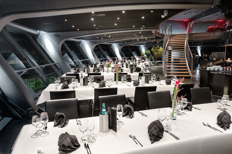 Restaurant Tische in Reihen, edle Bestuhlung, Gedeck für Gängemenü. Treppenaufgang zur historischen Fahrzeuggalerie im Hintergrund.