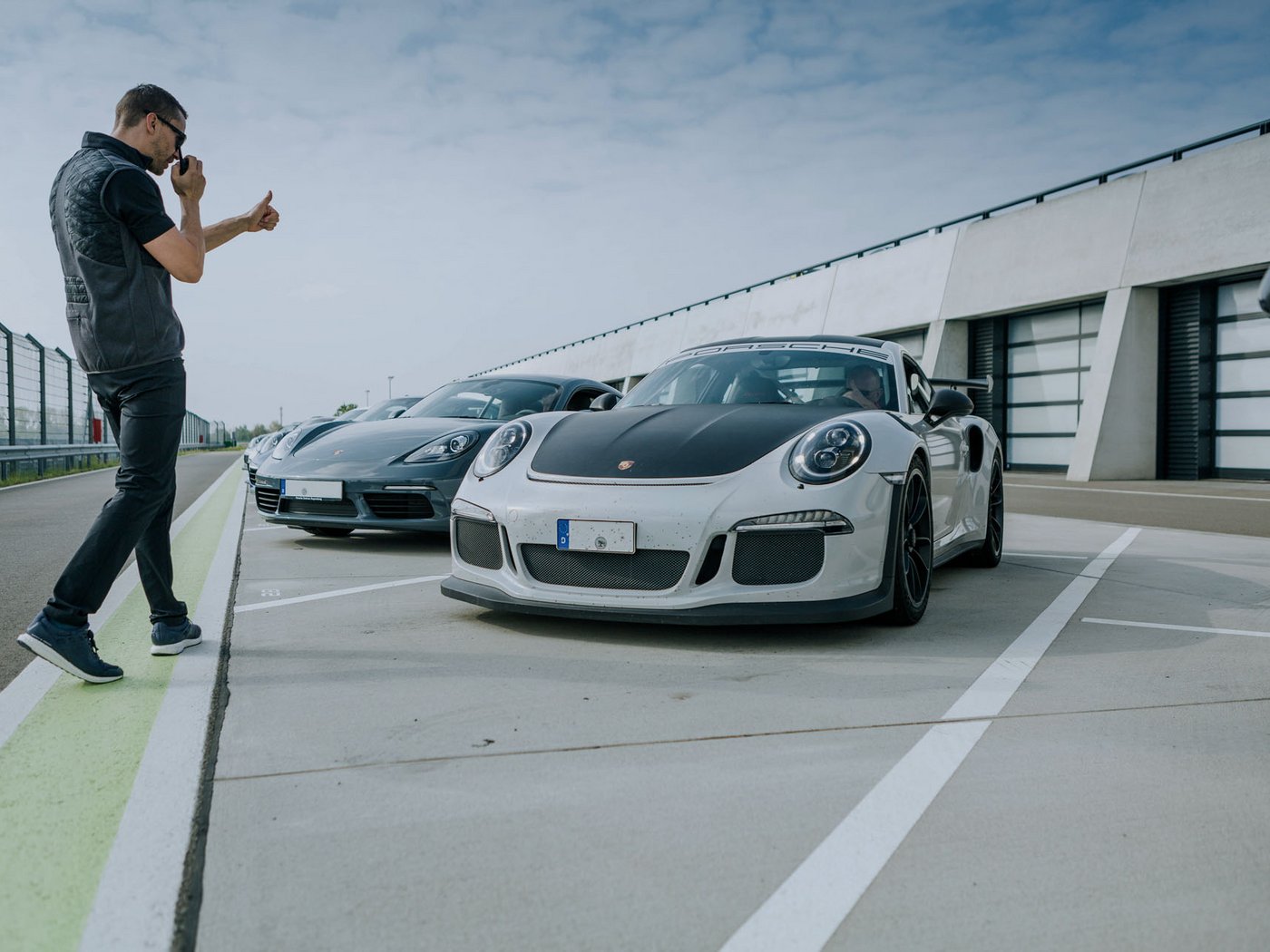 Ein Instrukteur steht in der Boxengasse des Porsche experience Center, Leipzig und interagiert mit einem Teilnehmer