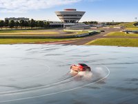 Porsche 911 Carrera S auf der bewässerten Fläche der Rundstrecke. Experience Center im Hintergrund.