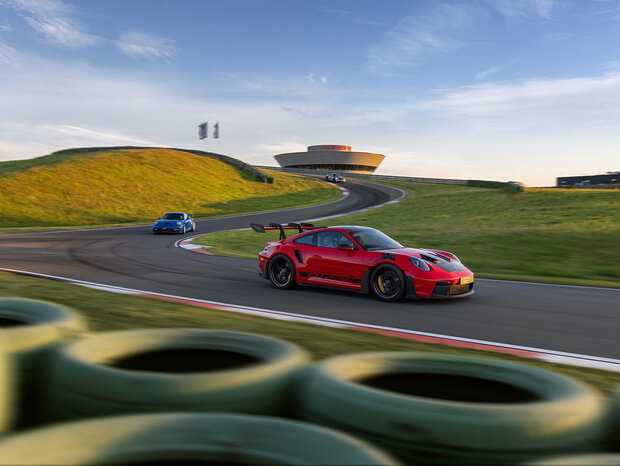 Mehrere Porsche Rennfahrzeuge fahren als Gruppe durch die Kurven der Rundstrecke.