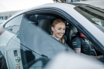 Eine Person sitzt auf dem Beifahrersitz eines Porsche neun elf und lacht in die Kamera