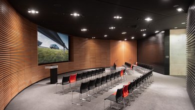 Große Leinwand, Rednerpult, Bestuhlung parlamentarisch. Raum mit Holz modern vertäfelt.