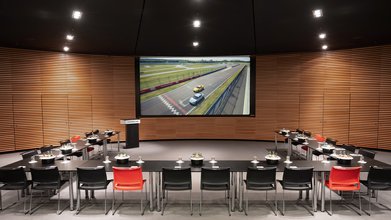 Große Leinwand, Rednerpult, Konferenz-Bestuhlung mit Tisch in U-Form. Raum mit Holz modern vertäfelt.