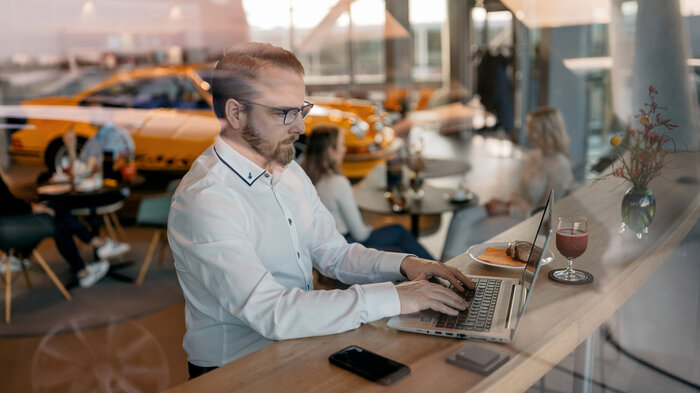 A man is sitting at a wooden bar in the Carrera Cafe, working on his laptop.