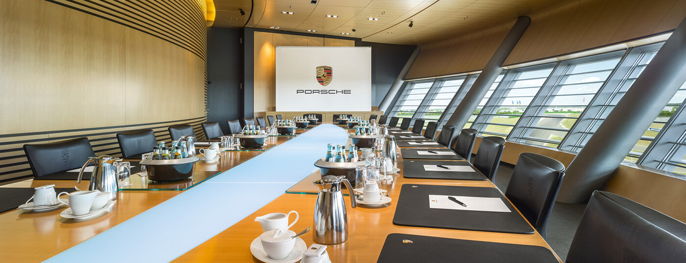 Large conference room. Long, wide solid wood table. Elegant leather chairs. Large screen. Modern wood paneling. Coffee service.