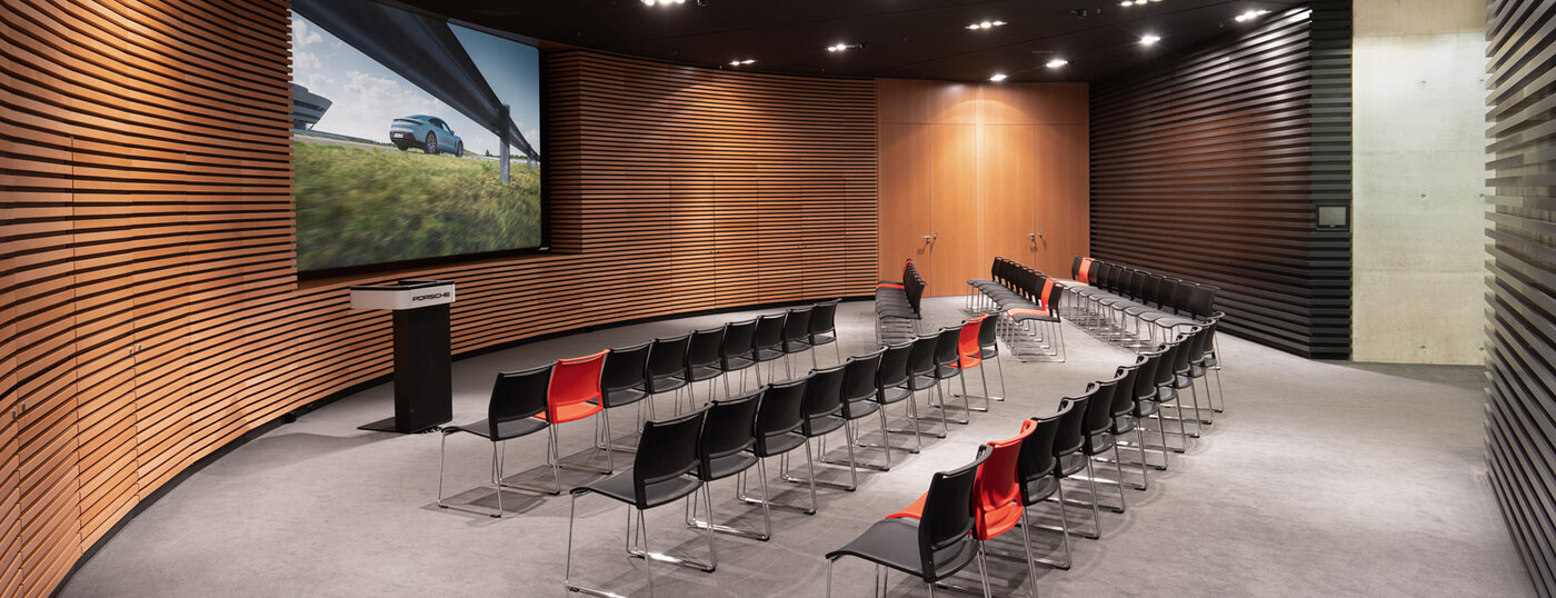 Large screen, lectern, parliamentary seating. Room with modern wood paneling.