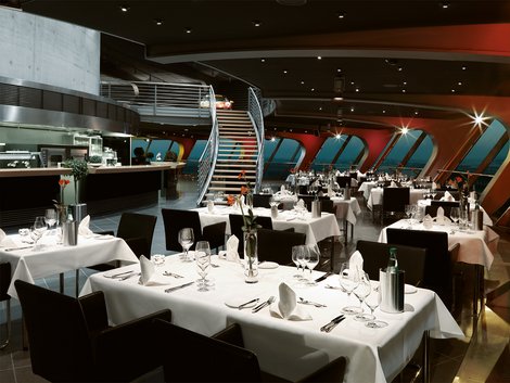 Tische in Reihen, edle Bestuhlung, Gedeck für Gängemenü. Treppenaufgang zur historischen Fahrzeuggalerie im Hintergrund.