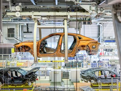 Eine Karosserie des Porsche Macan hängt an einer speziellen Hängevorrichtung von der Decke des Werksgebäudes. Sie ist fahrbar und bewegt sich Schritt für Schritt durch die Produktion in der Fabrik.