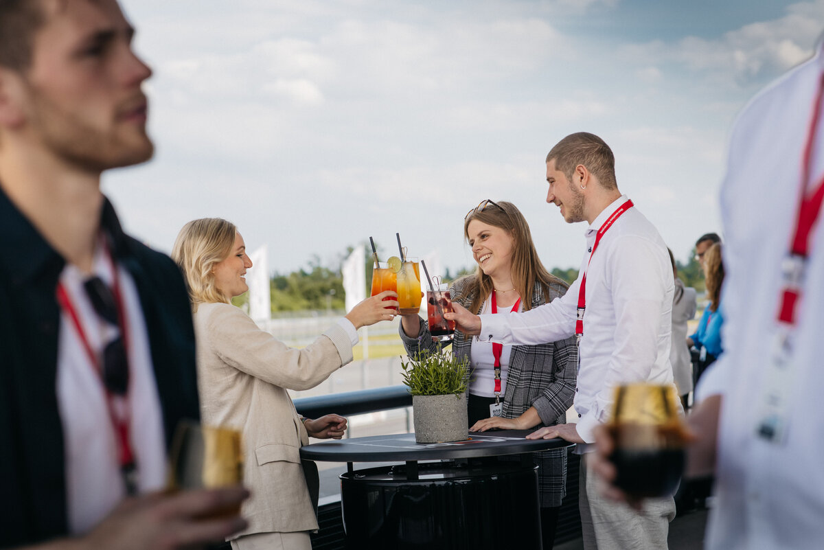 Stehtisch mit drei Personen, die sich zuprosten mit Getränken.