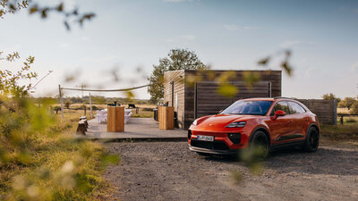A Cayenne stands in front of the off-road terrain at sunset. There is plenty of nature to see and a modern wooden hut, which is the meeting point for the off-road terrain.