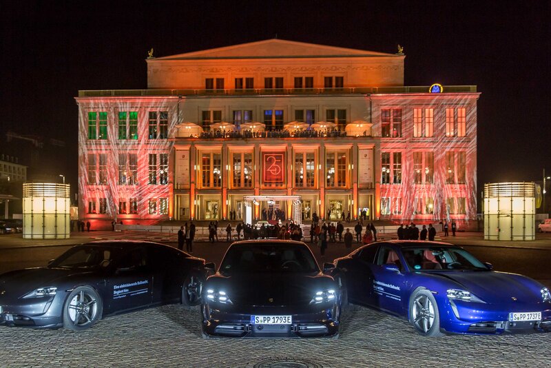 Die Oper ist von außen bei Nacht zu sehen. Sie wird angestrahlt. Davor steehn aufgereit drei Porsche Taycan. 