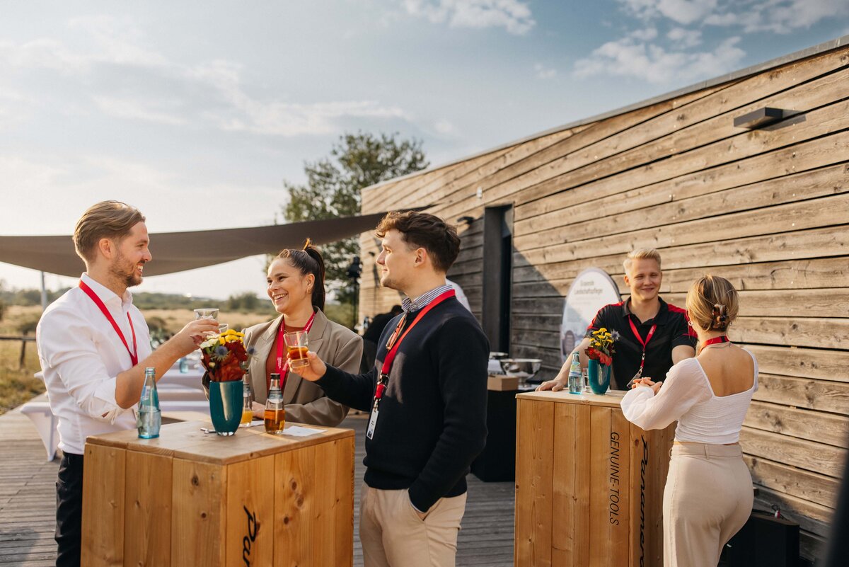Several people are standing around high wooden tables enjoying drinks.