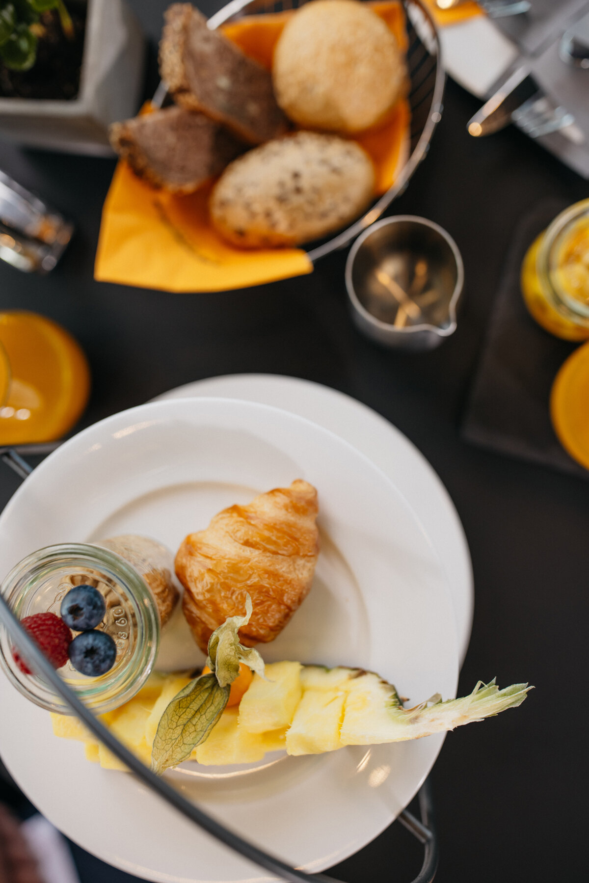 geschnittene Ananas. Müsli mit Heidelbeeren und Himbeeren. Diverse Brötchen und Croissants.