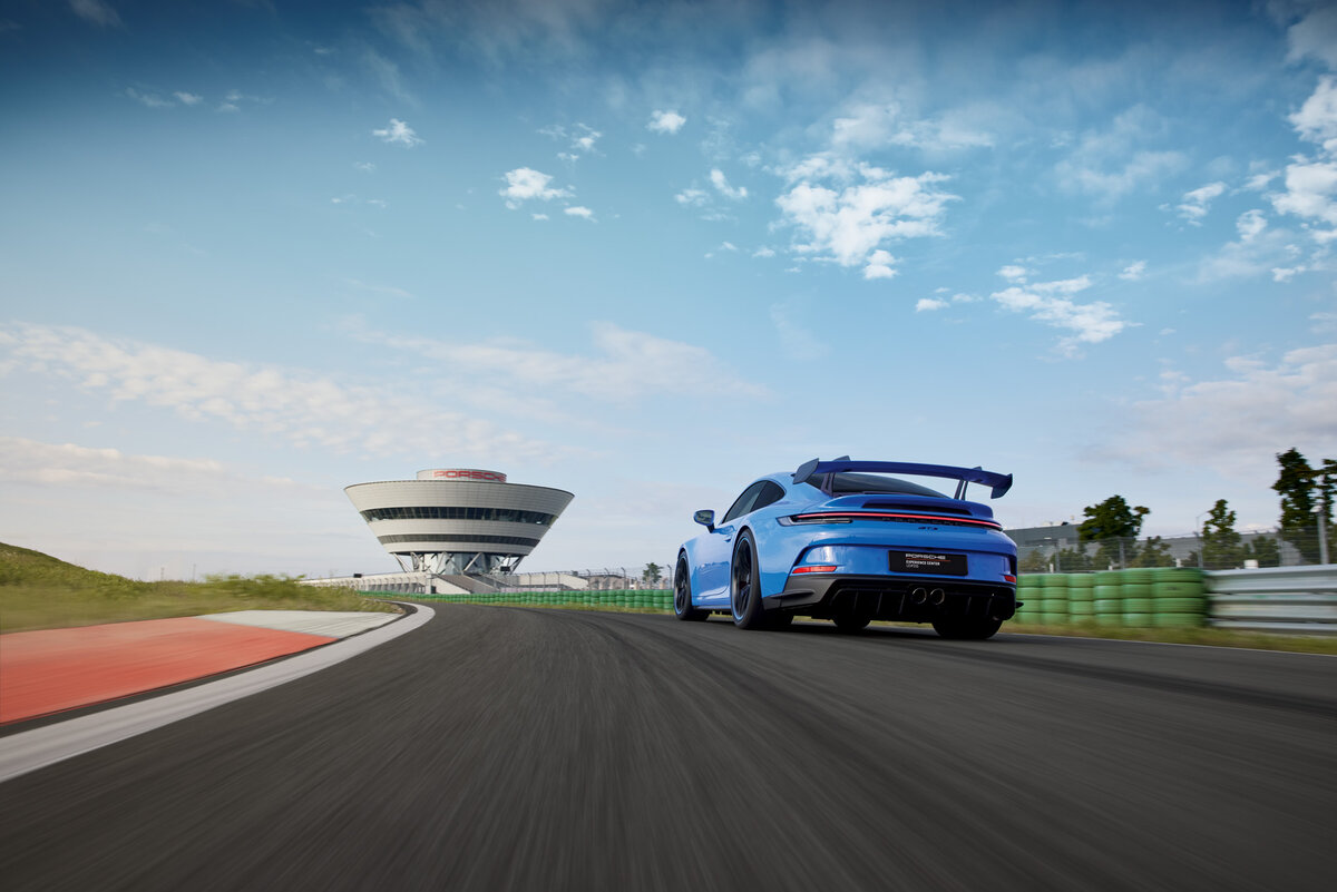 Ein Porsche 911 auf der Rheinstrecke und im Hintergrund das Porsche experience Center
