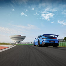 Ein Porsche 911 auf der Rheinstrecke und im Hintergrund das Porsche experience Center