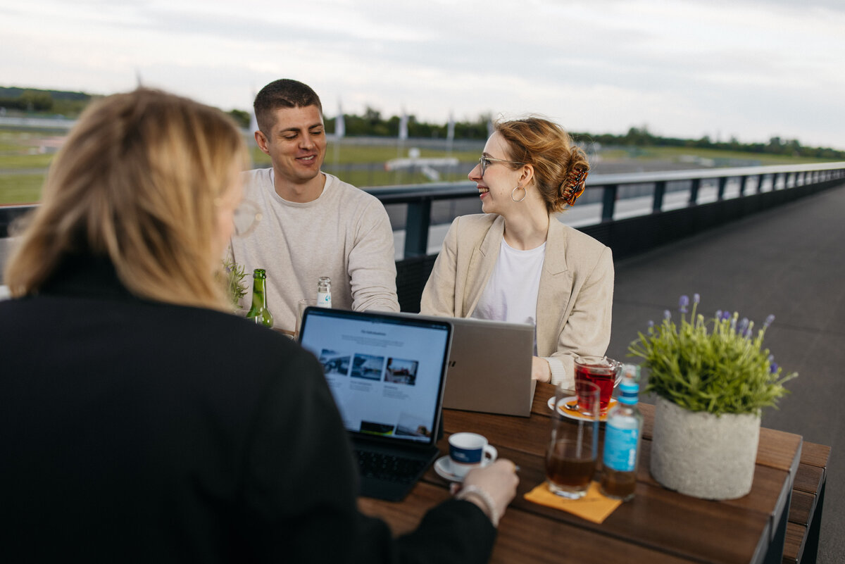 Terrassentische mit Bänken. Mehrere Personen arbeiten an ihren Laptops zusammen. 