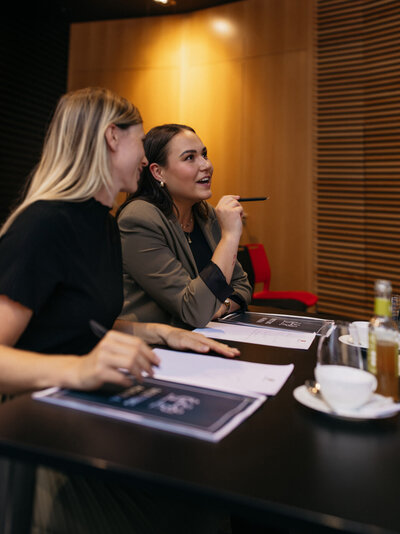 Zwei junge Frauen sitzen an einem Konferenztisch.