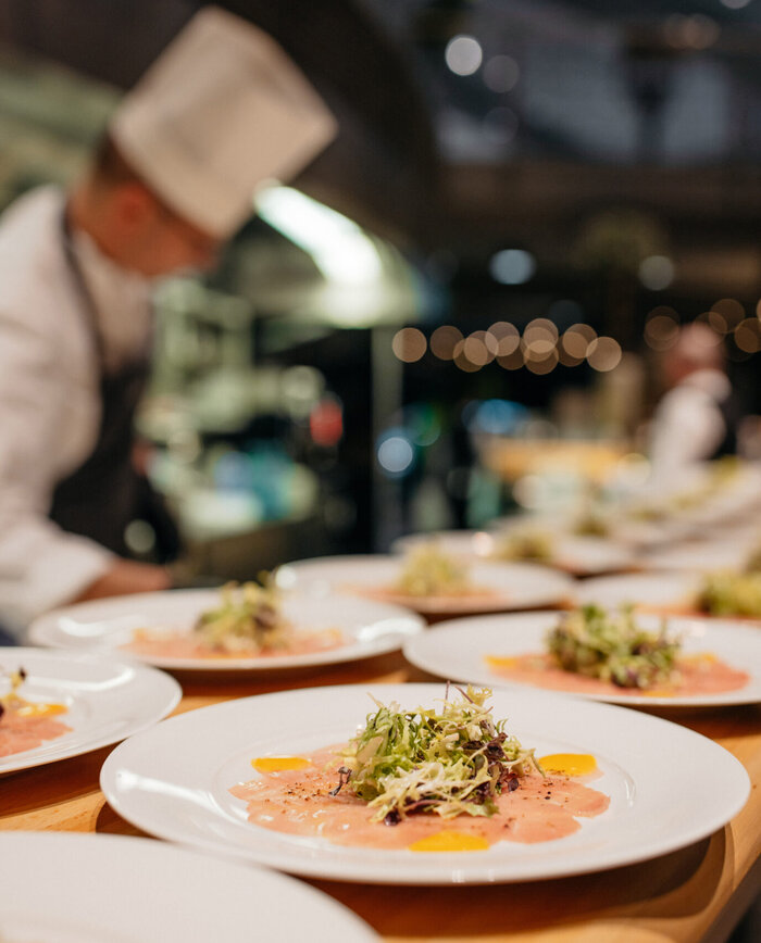 A chef prepares several plates of carpaccio. It is high quality and looks beautifully garnished.