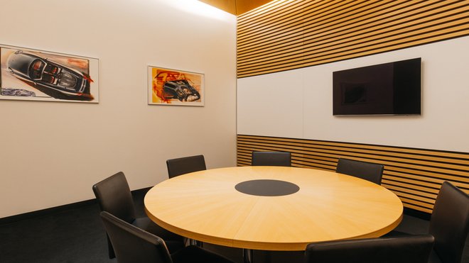Runder Tisch, Platz für 8 Personen. Bildschirm an der Wand.
