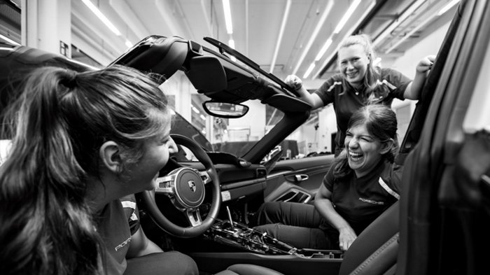 junge Auszubildene stehen lachend um ein 911er Cabrio.