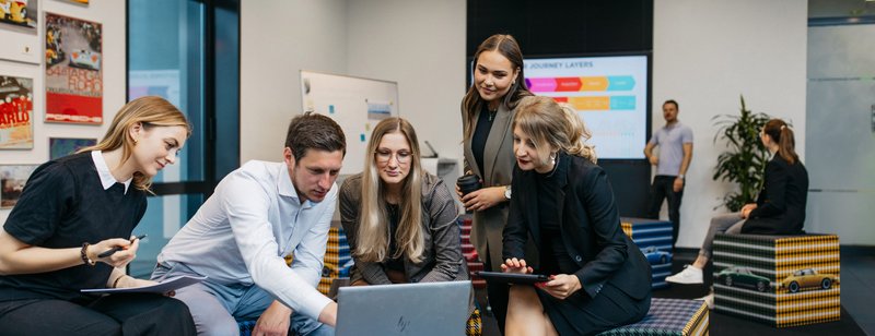 mehrere Personen sitzen um einen Laptop herum und unterhalten sich. 