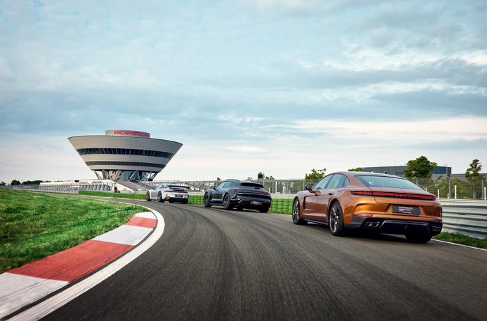 Bild Fahrerlebnis. Zwei Porsche Panamera und ein Taycan fahren hintereinander auf der Rundstrecke. Im Hintergrund ist das Experience Center zu sehen.