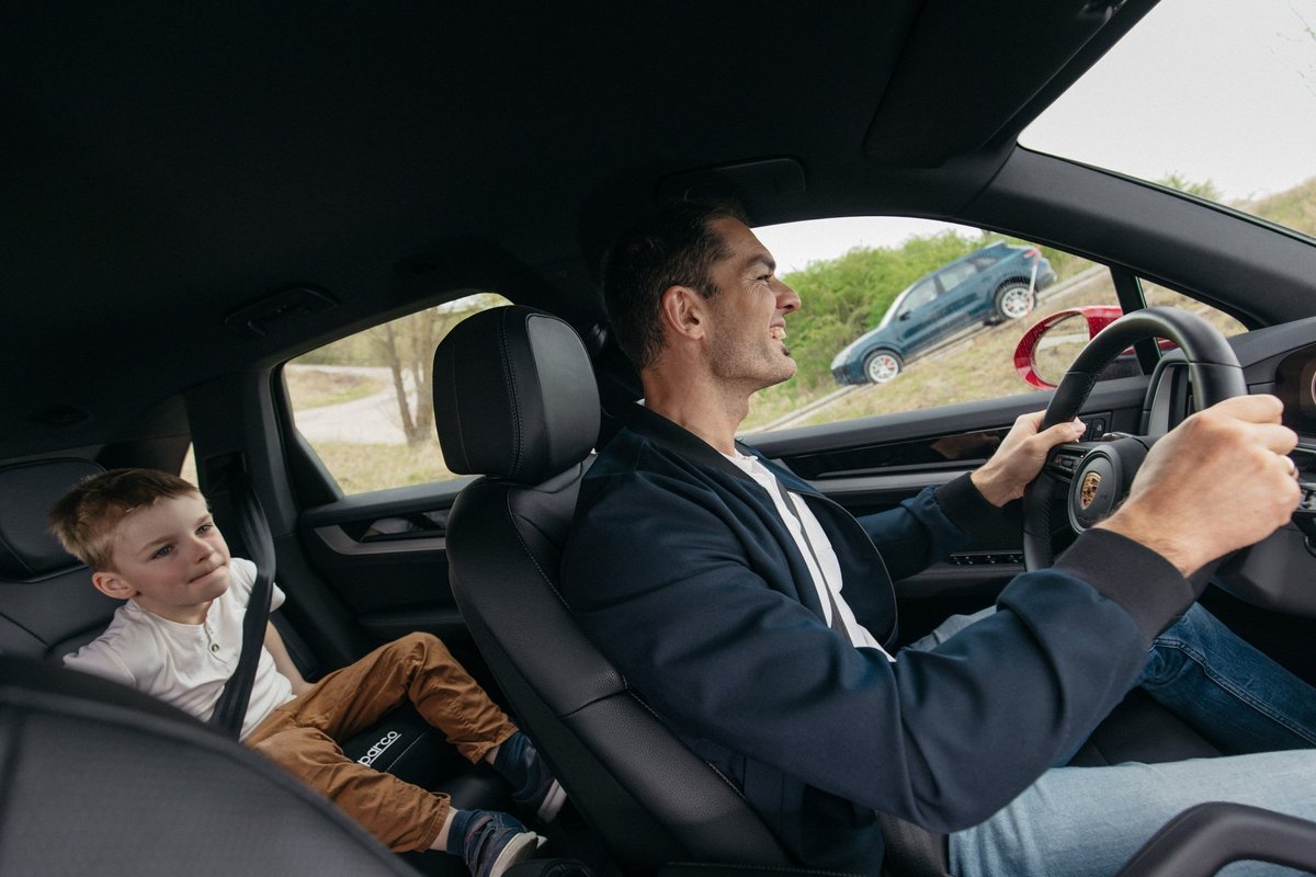 Ein Mann steuert den Porsche Cayenne und das Kind auf der Rücksitzbank sieht dabei zu