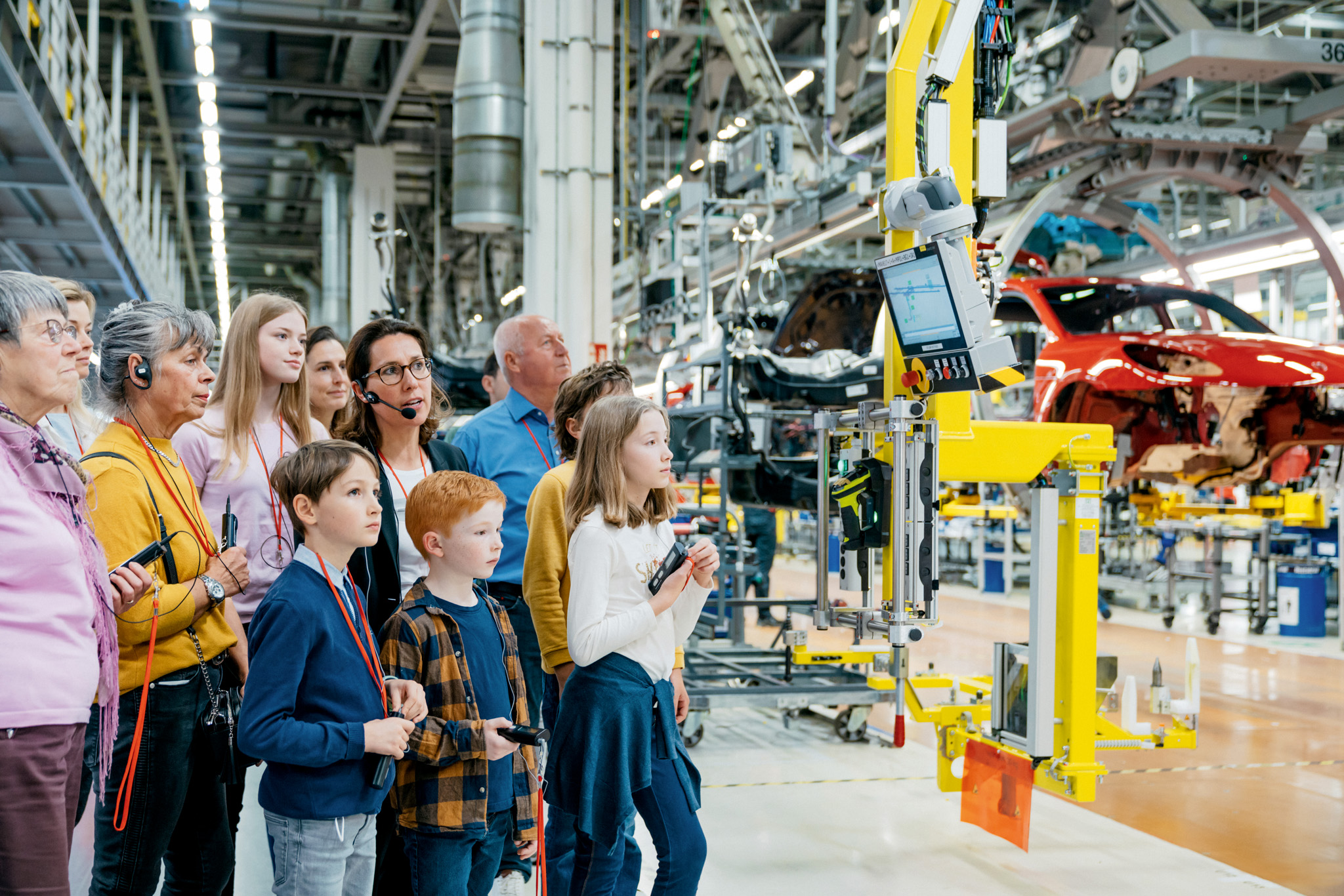 Zwei Familien mit Kindern und Großeltern sind bei einer Werksführung. Sie beobachten einen Produktionsschritt im Porschewerk. 